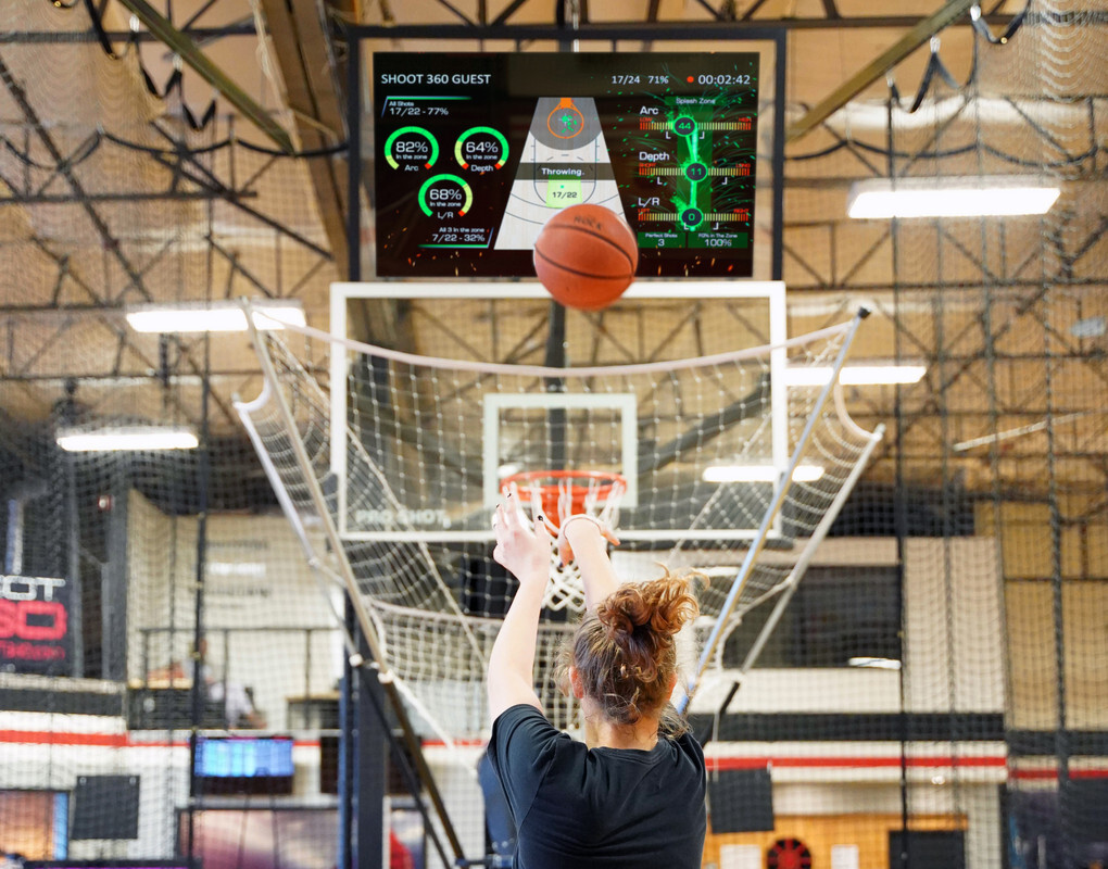 Basketball player takes a shot on a Shoot 360 training court while a digital screen displays real-time shooting metrics above the hoop.